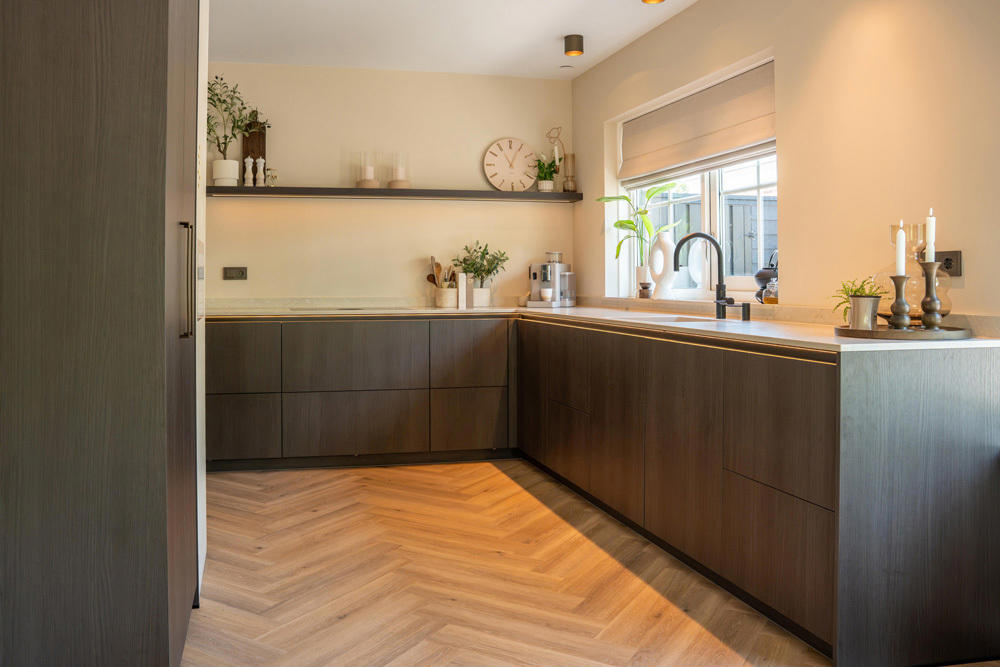 Donkerbruine houten keuken met lichte werkbladen, greeploze fronten, zwarte kraan en warme ledverlichting